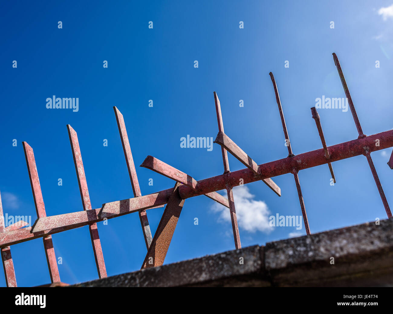 Red metal spiked security barrier against a blue sky. Stock Photo