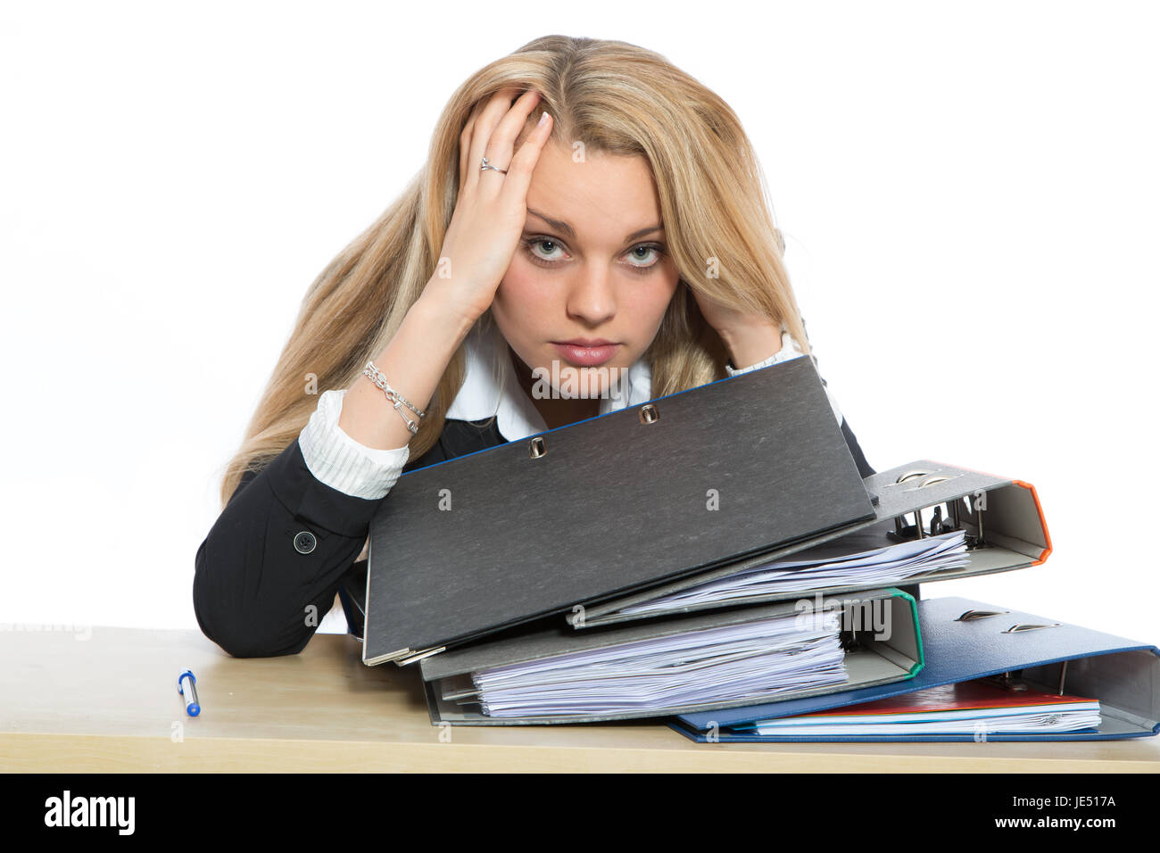 Junge Frau sitzt am Schreibtisch über einen Stappel mit Aktenordnern und blickt gefrustet. Stock Photo