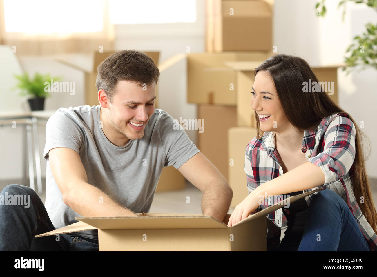 Couple moving home packing belongings in a cardboard box sitting on the floor of the living room Stock Photo