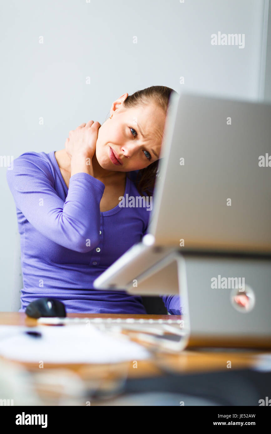 Working too hard - young woman working on a computer at an office, having sore back, being overloaded with work, sitting too much, putting too much stress on her eyes,.. Stock Photo