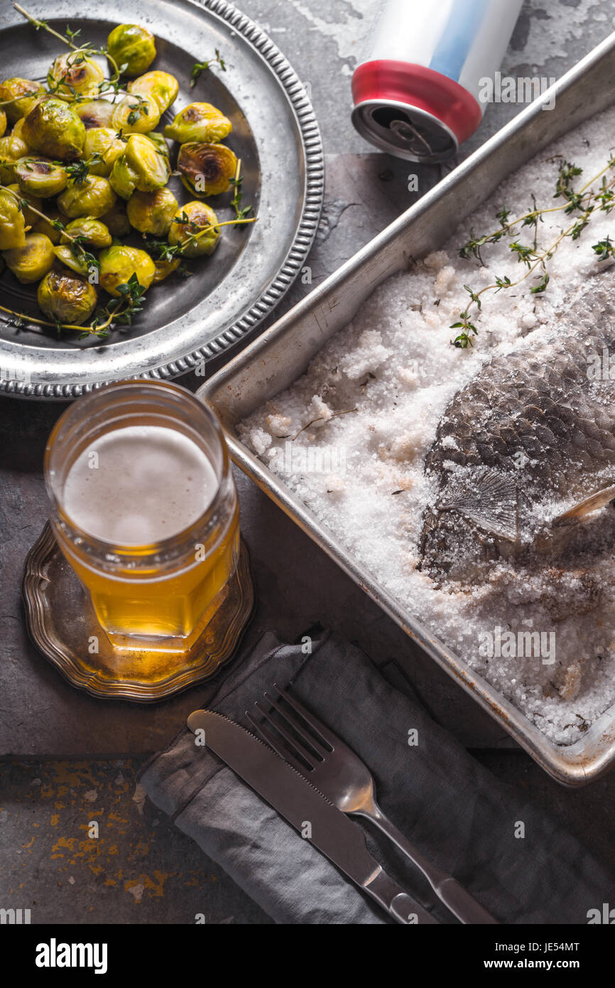 Fish baked in salt with Brussels sprouts and beer vertical Stock Photo