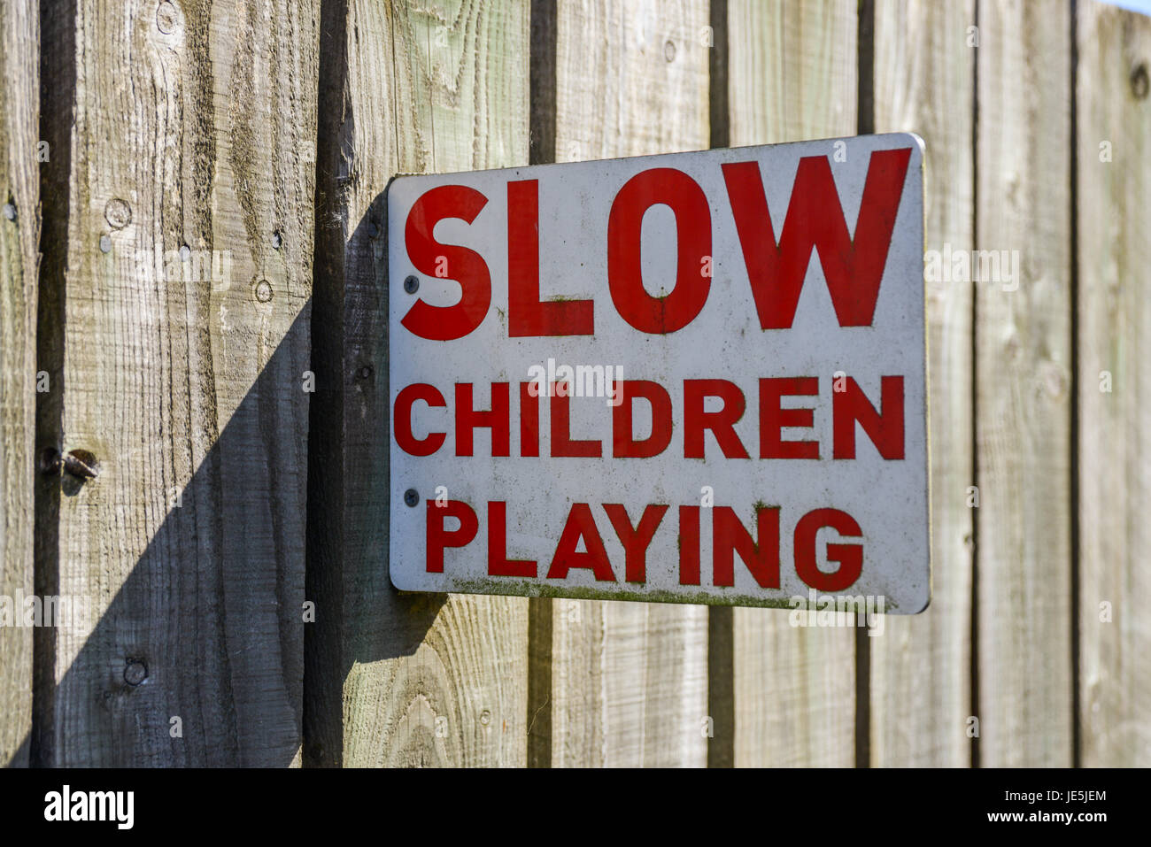 'Slow Children Playing ' sign mounted to wooden fence. Stock Photo
