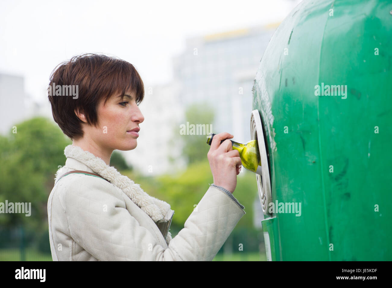 Woman putting wine bottle into recycling bin Stock Photo