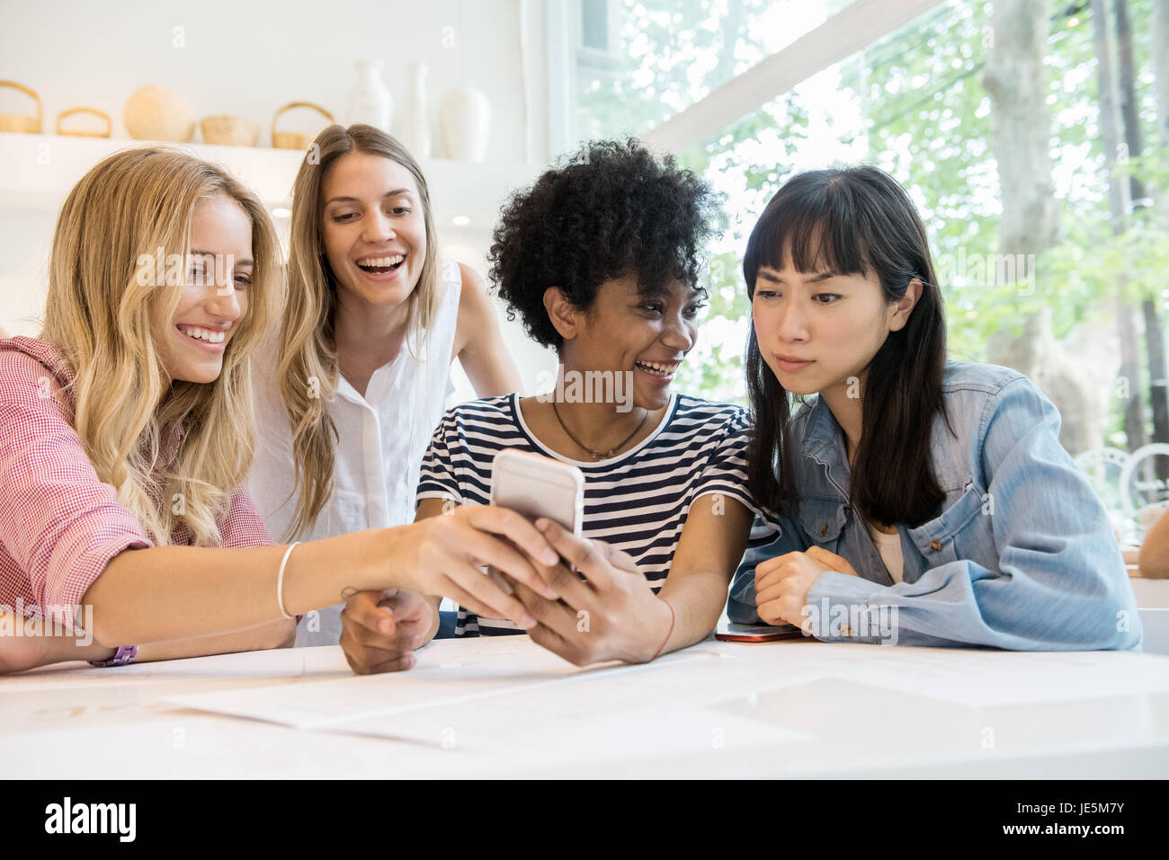 Young women laughing at multimedia smartphone in cafe Stock Photo