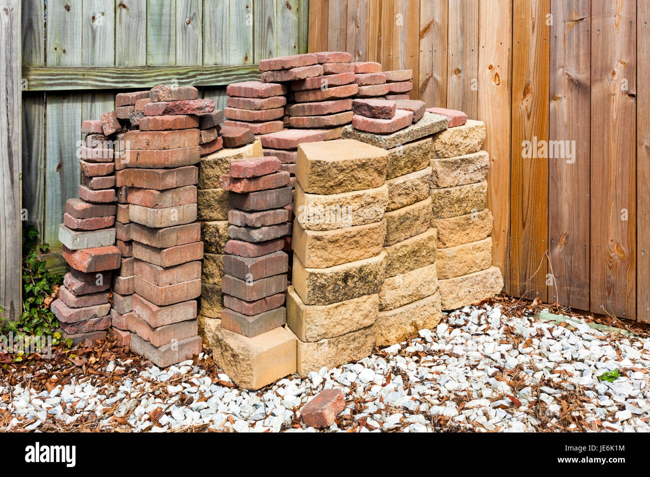 Used bricks and paving stones stacked against wood fence with white gravel foreground. Horizontal. Stock Photo