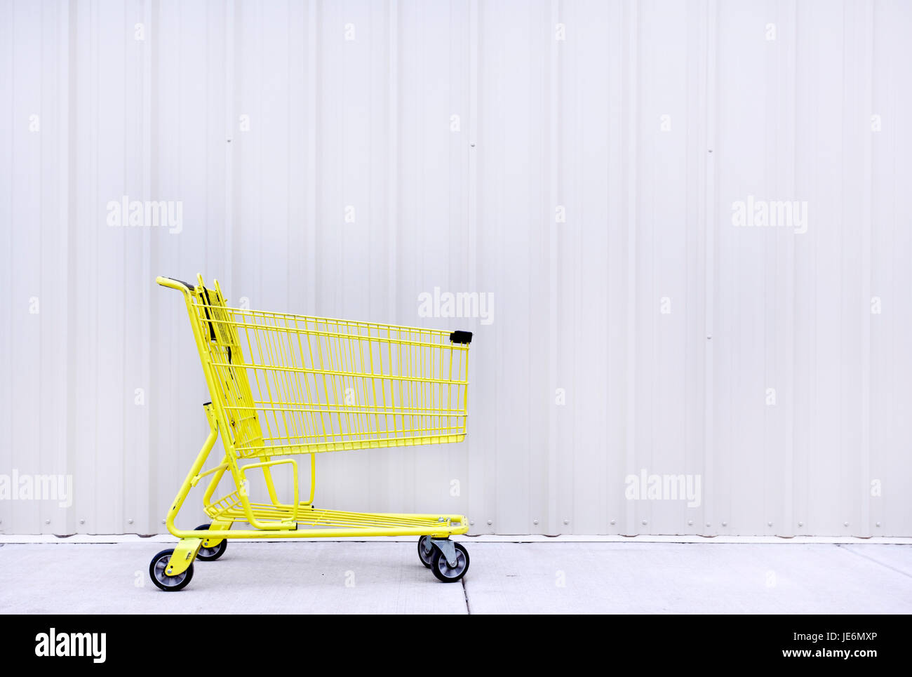 Yellow shopping cart on sidewalk against grey / gray wall. Horizontal