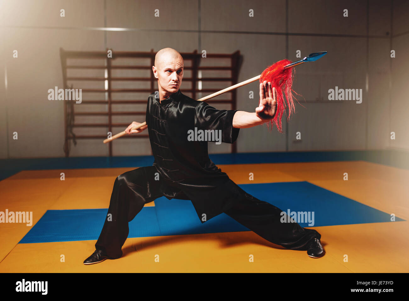 Wushu master training with spear, martial arts. Man in black cloth poses with blade Stock Photo