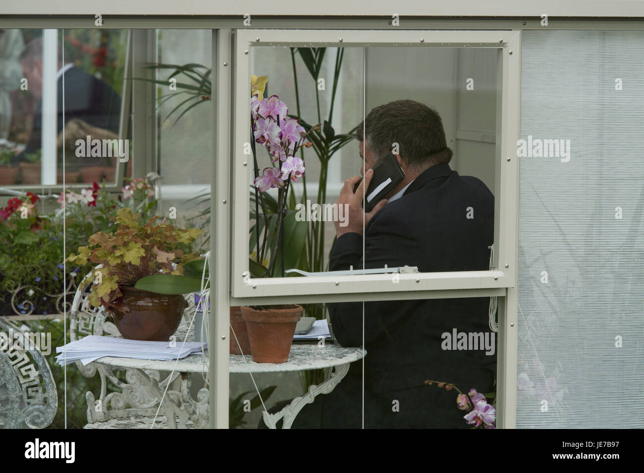 Salesman on phone, sits in display greenhouse on Hartley Botanic trade stand - RHS Chatsworth Flower Show, Chatsworth House, Derbyshire, England, UK. Stock Photo