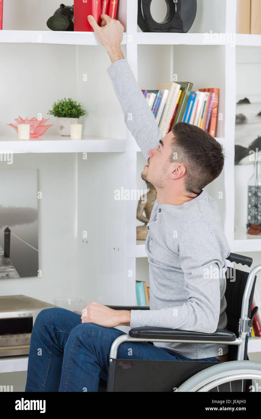 Young man in wheelchair reaching to high shelf Stock Photo Alamy