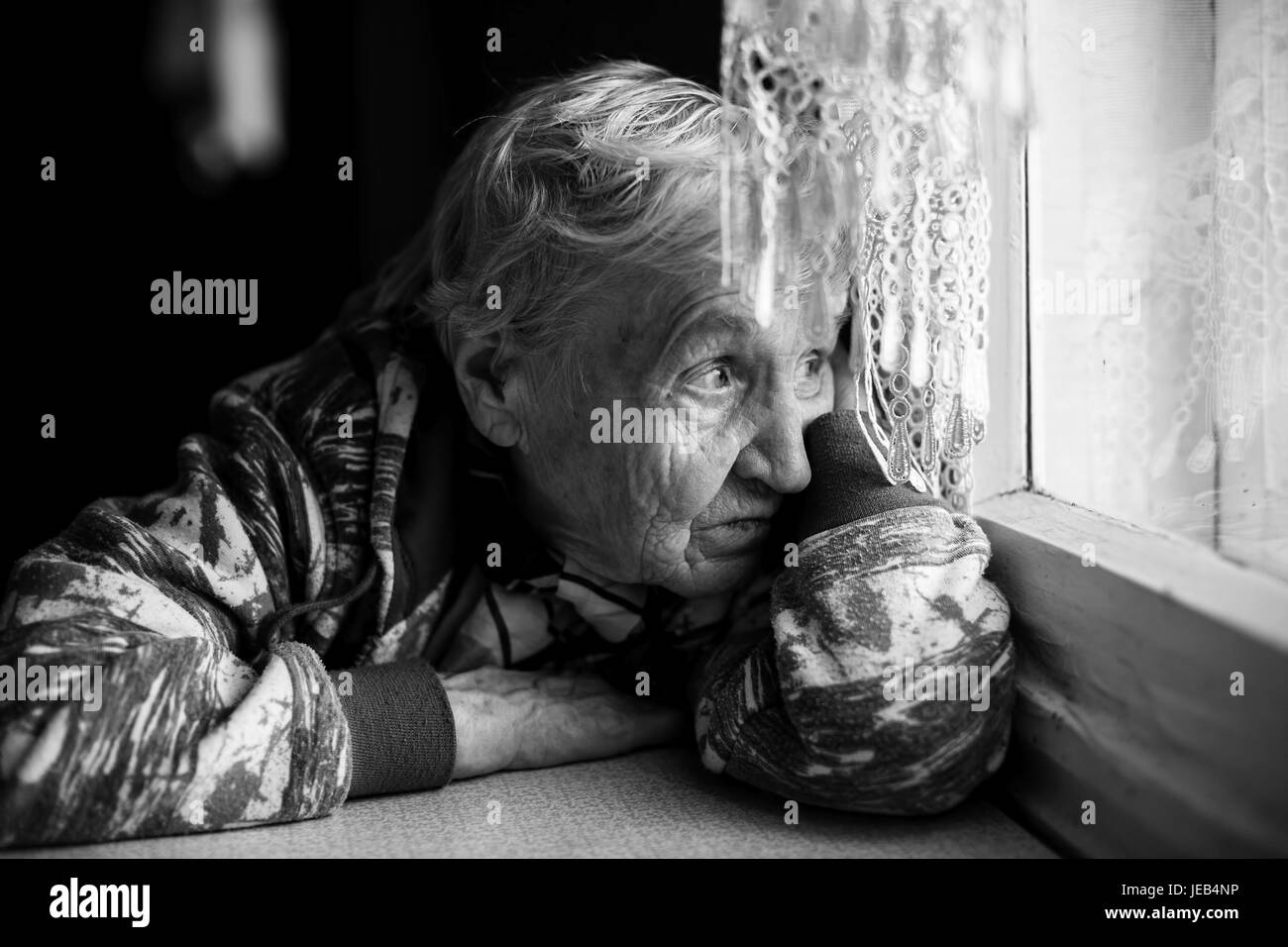 An elderly woman looks wistfully out the window. Black-and-white photo. Stock Photo