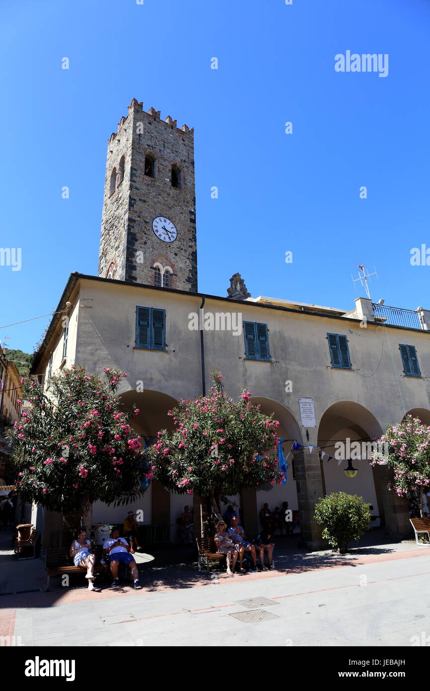 Clock tower in the centre of the village of Monterosso, one of the villages in the famous 'Cinque Terre', with shady seating area under flowering bush Stock Photo