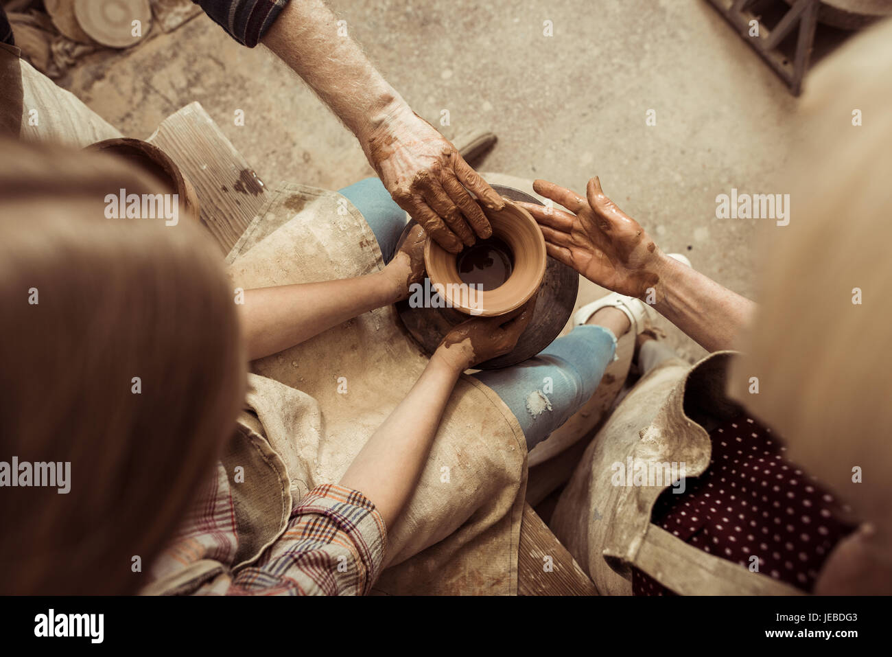 Overhead view of little girl making pottery on wheel with help of grandparents at workshop Stock Photo