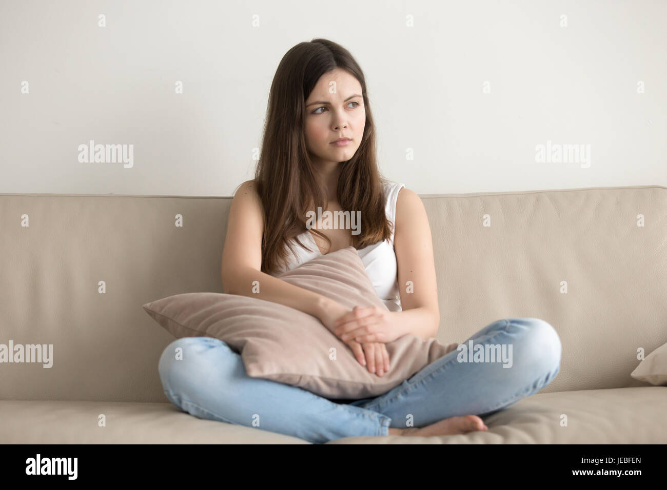 Concerned young woman sitting on sofa at home Stock Photo