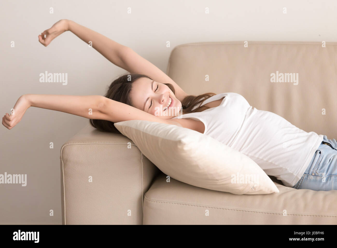 Happy young woman stretches on sofa after nap Stock Photo