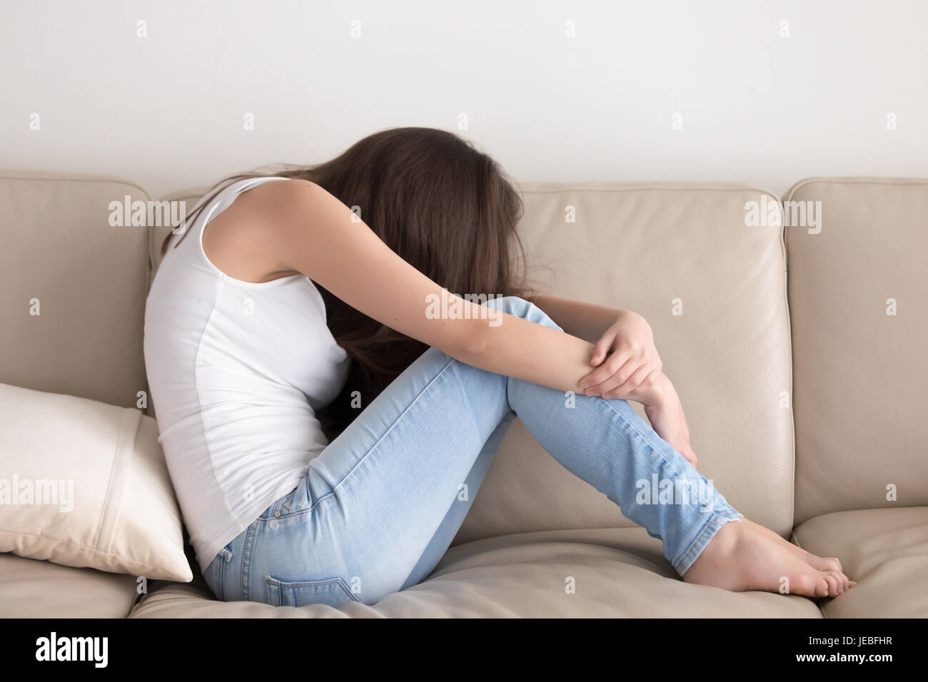 Depressed teen sitting on sofa and embracing knees Stock Photo