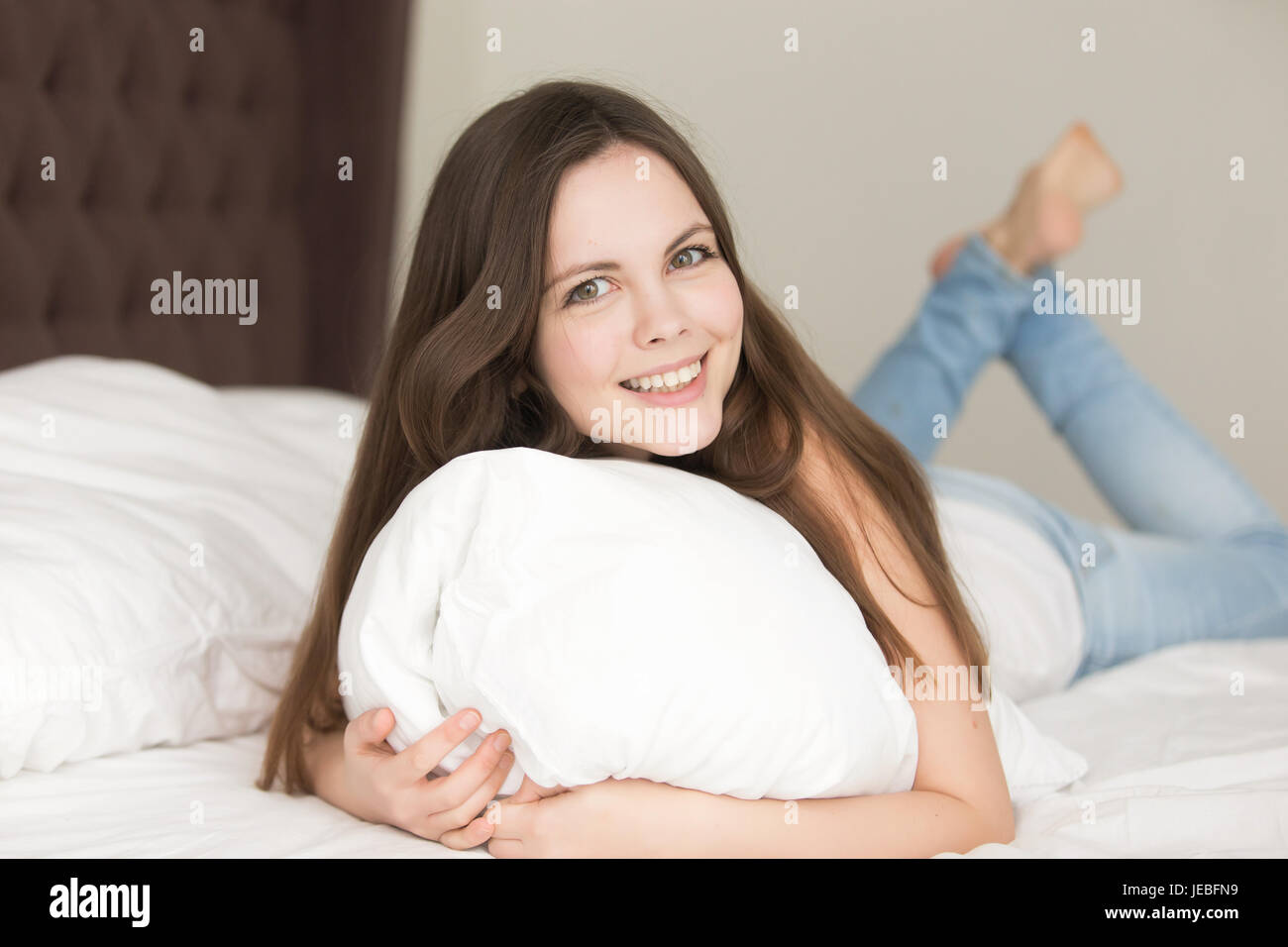 Relaxed young woman lying in bed on stomach Stock Photo