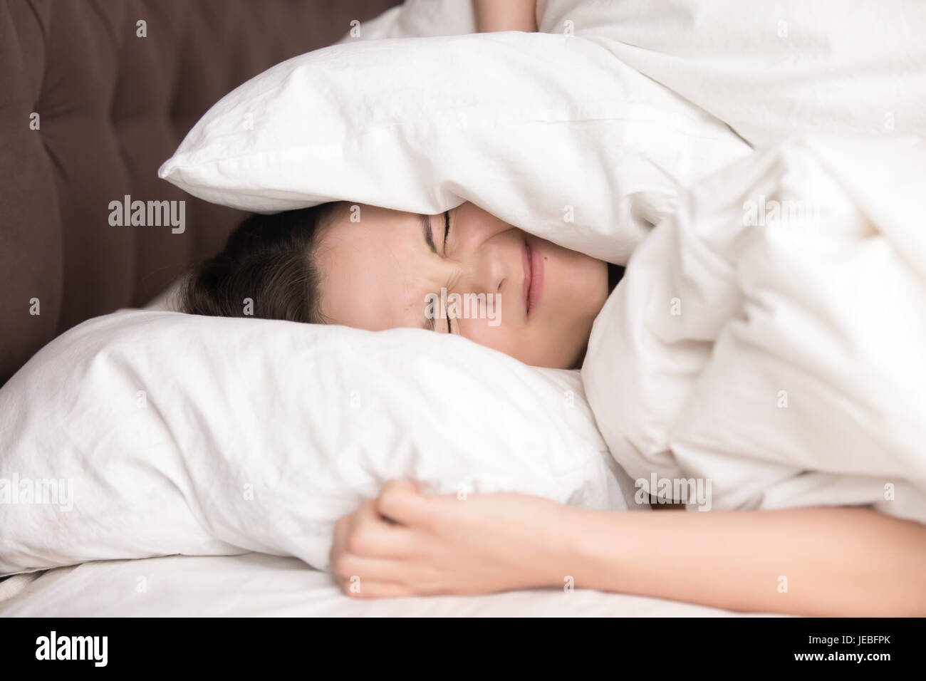 Woman covering head with pillow because of noise Stock Photo