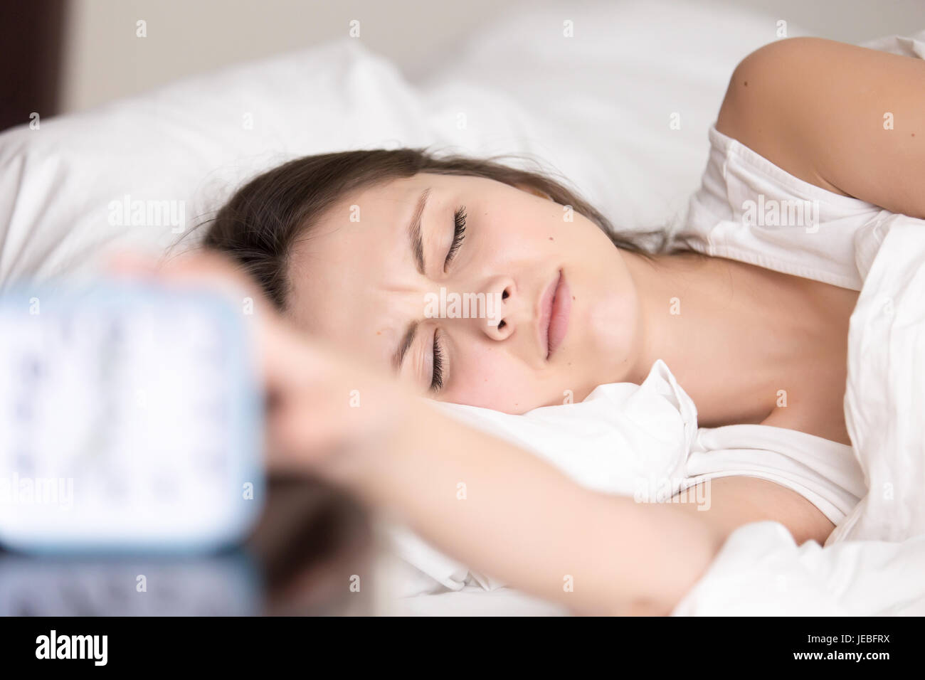 Sleepy young woman turns off signal of alarm clock Stock Photo