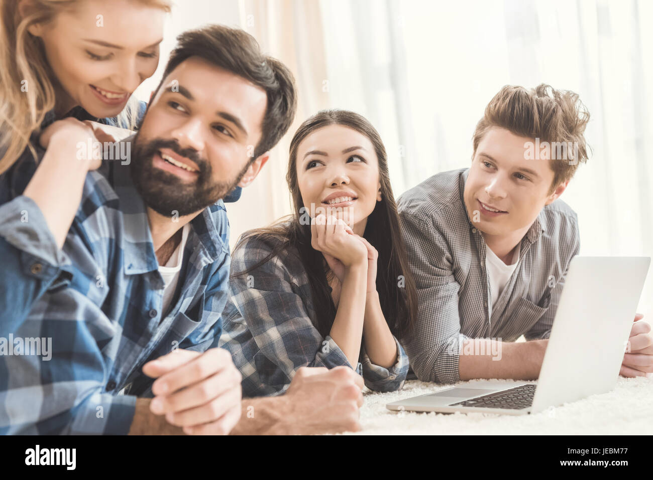 Two young couples lying on floor, having fun and using laptop Stock ...