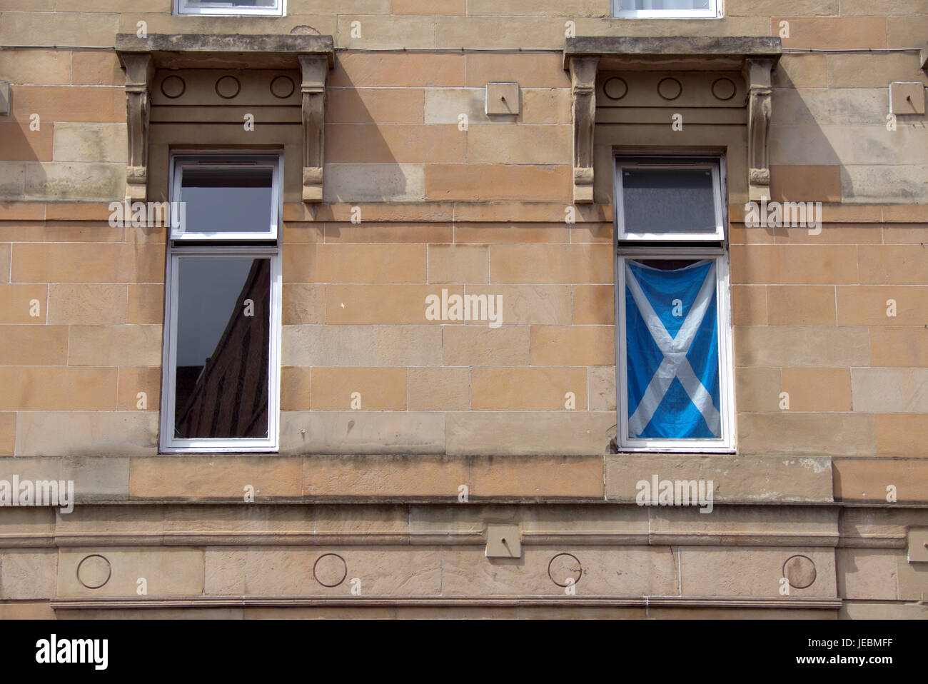 Scottish tenement windows with reflection of sandstone building and satire flag in the window Stock Photo