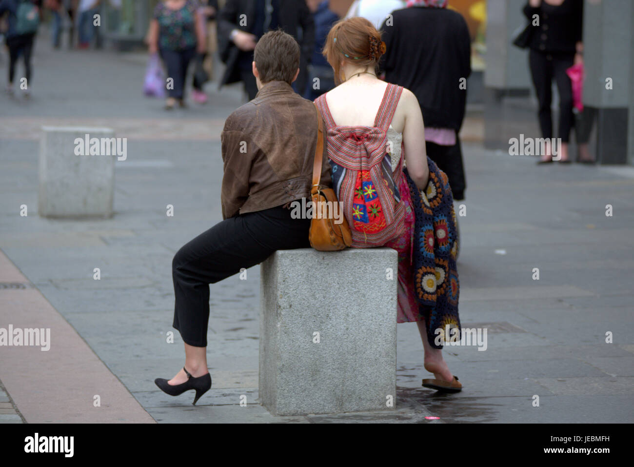 two Glasgow ladies having a rest sitting astride on a street bollard women sitting down watching life go by on Argyle Street Glasgow City centre Stock Photo