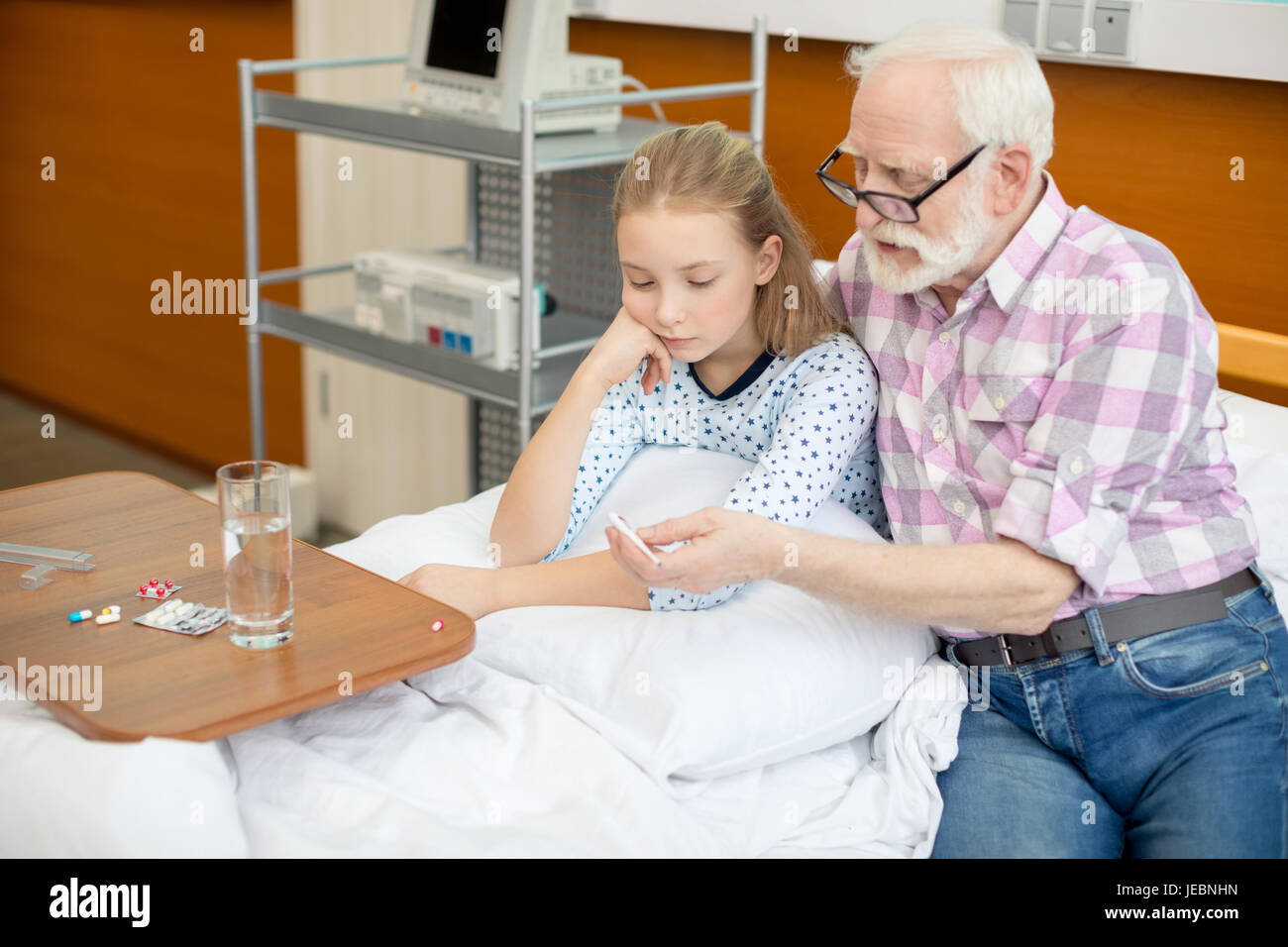 Senior man in eyeglasses and sick little girl looking at thermometer in