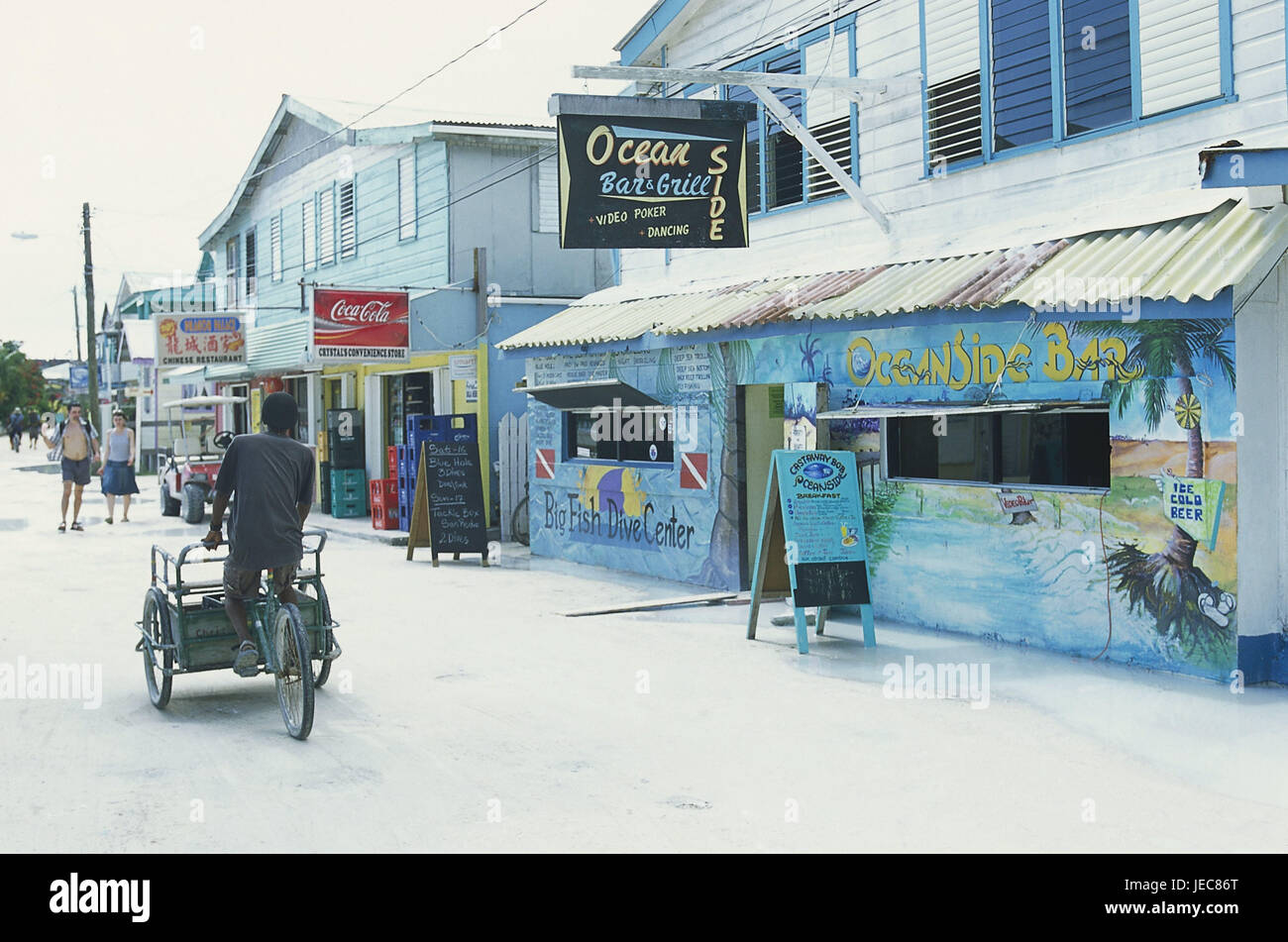 Belize, island Caye Caulker, shopping street, cyclist, tourist, no model release, Central America, destination, place, tourism, building, shops, street, passer-by, pedestrian, person, man, bicycle, bars, bars, restaurants, advertisement signs, Stock Photo