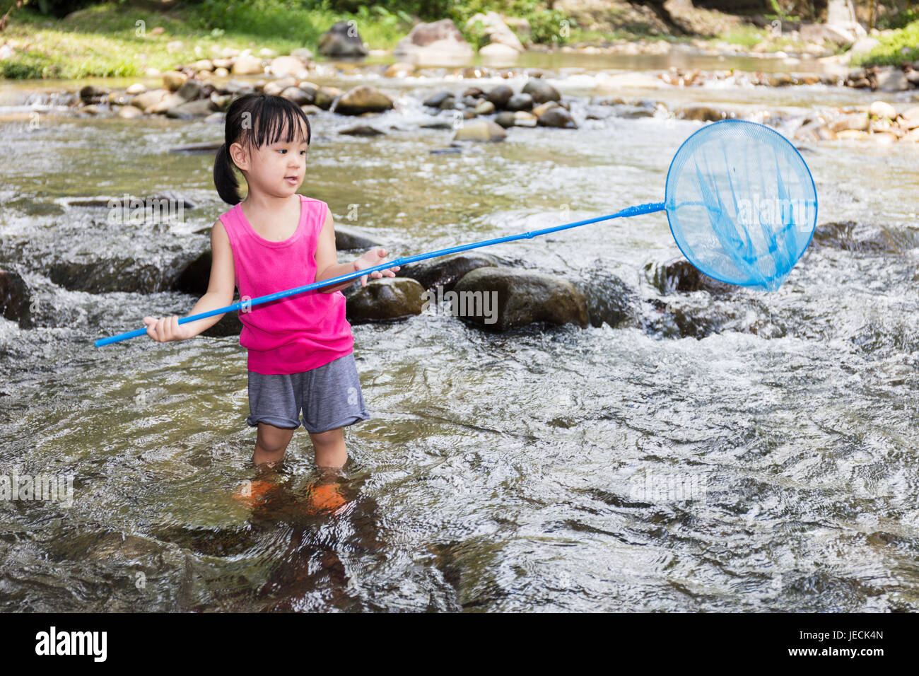 Asian Chinese little girl catching fish with fishing net in the creek. Stock Photo