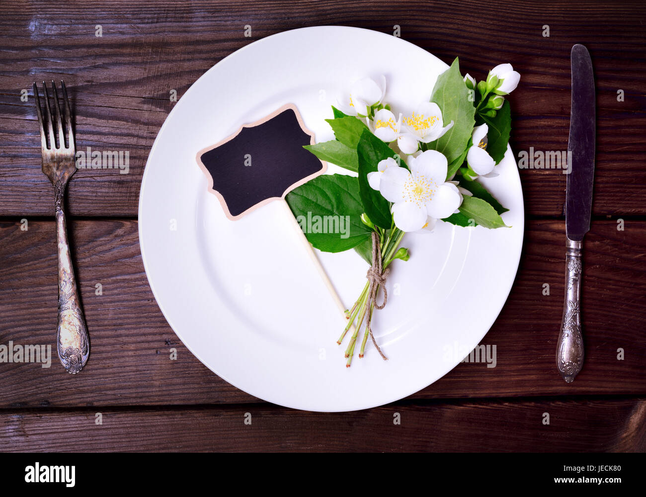 White round plate with iron knife and fork on a brown wooden background, top view Stock Photo