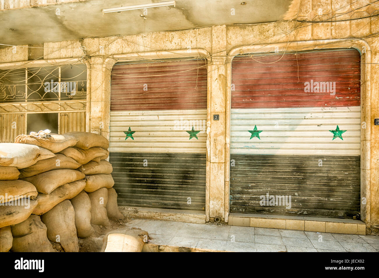 Sandbags blocking the sidewalk and garage doors painted like the Syrian flag in Hasakeh, Syria. Stock Photo