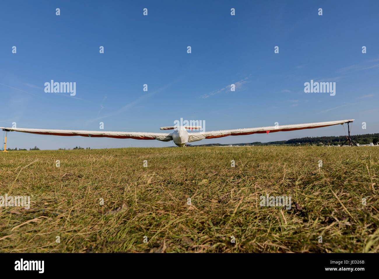 A glider with a protective sleeve parked on a grassy airport on a sunny day. Stock Photo