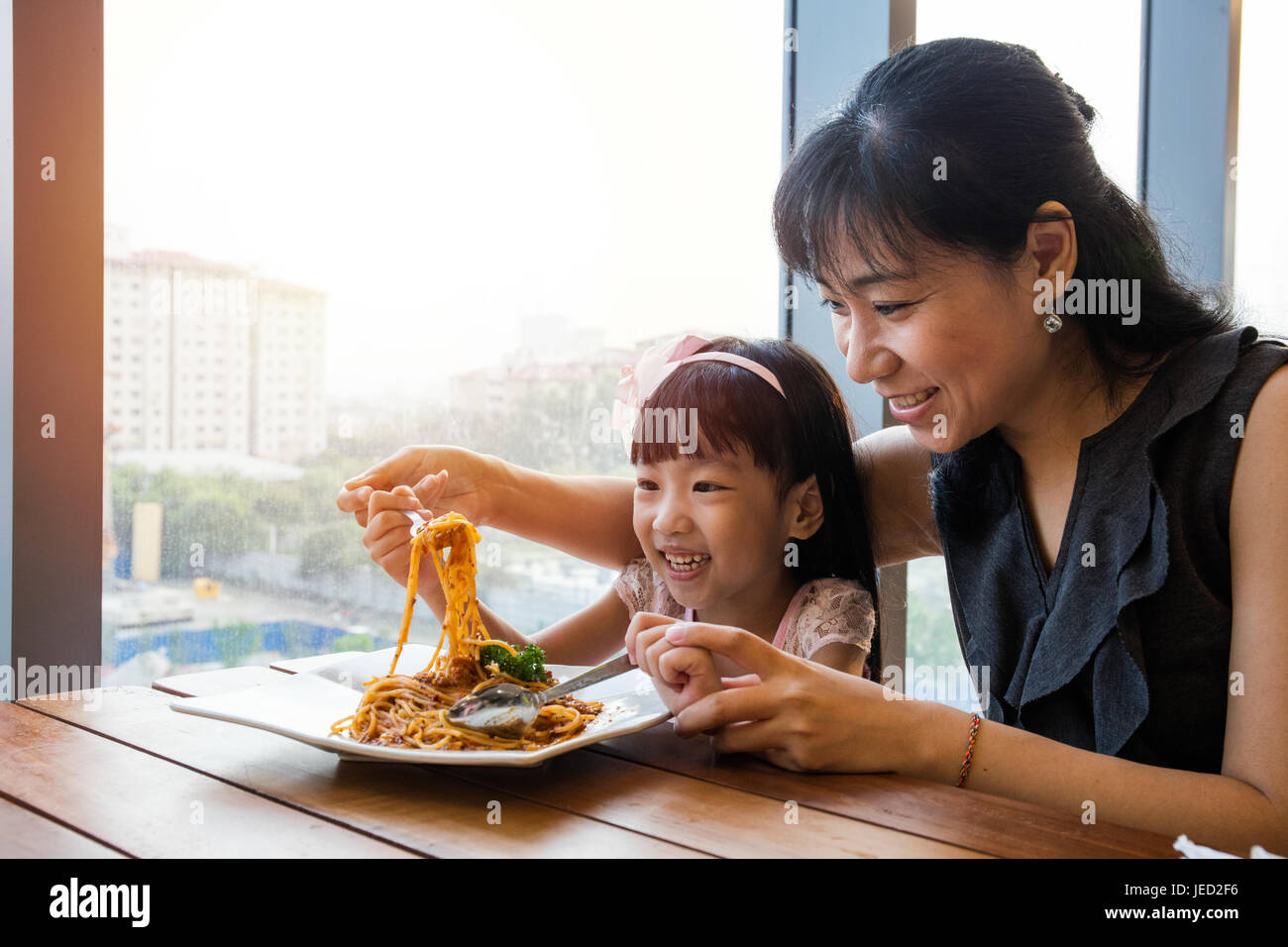 Asian Chinese mother and daughter eating spaghetti bolognese in the restaurant. Stock Photo