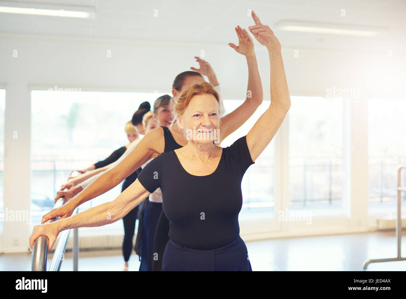Senior adult woman standing with hand up performing a dance in ballet class. Stock Photo