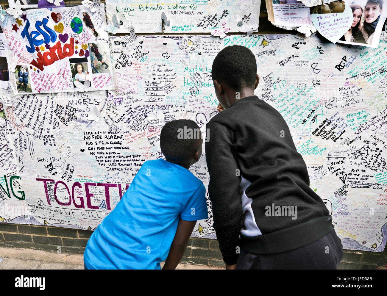 Families and friends writing on the wall of condolence in the aftermath of the fire that destroyed the 24-story Grenfell Tower in North Kensington, London on 14th June 2017.  The death toll officially at 75 but will no doubt rise to three figures. Stock Photo