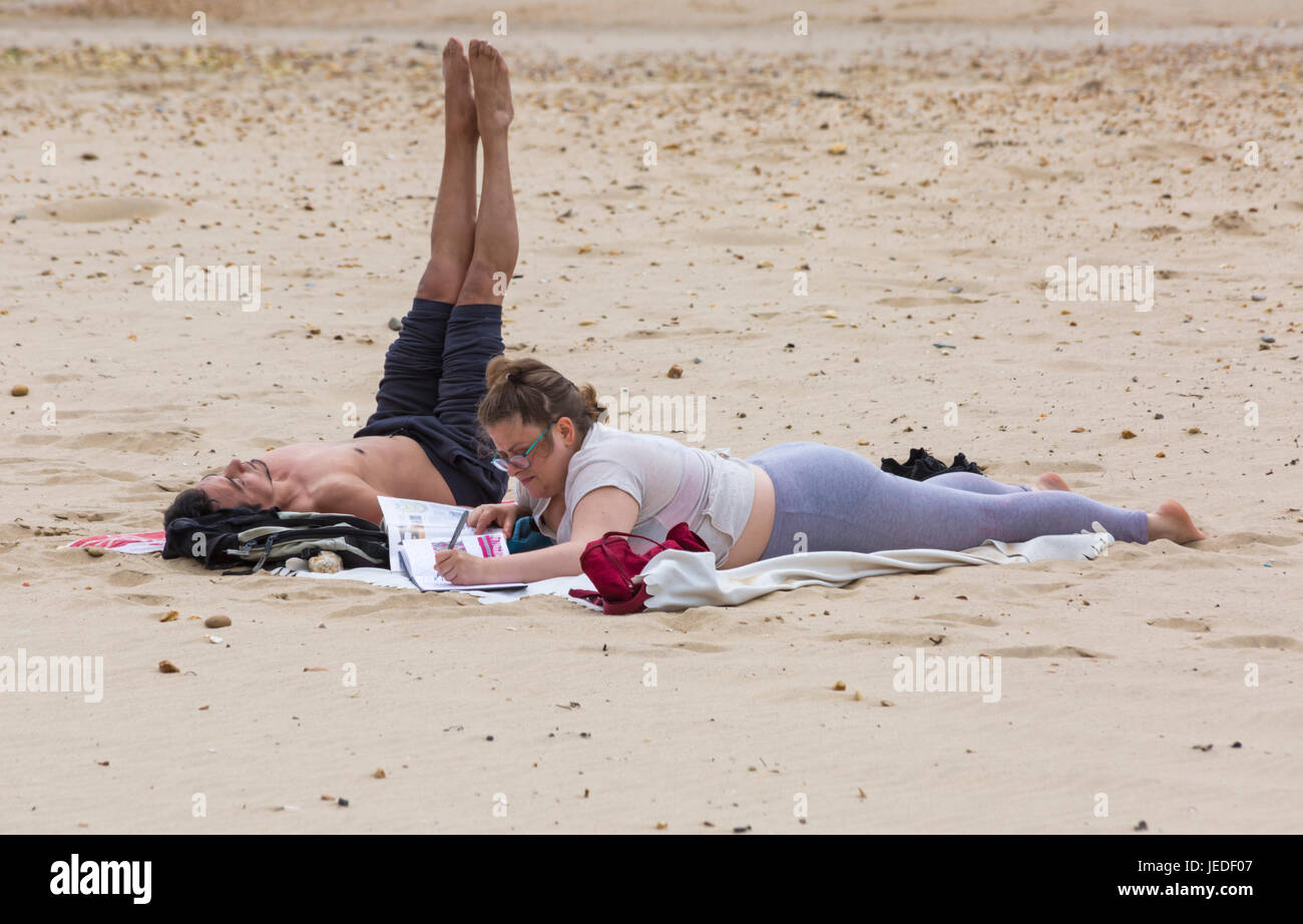 Bournemouth, Dorset, UK. 24th June, 2017. UK weather: overcast day with cooling breeze and sunny spells, as visitors head to the seaside. Couple on the beach, woman looking at magazine book, man doing exercises. Credit: Carolyn Jenkins/Alamy Live News Stock Photo