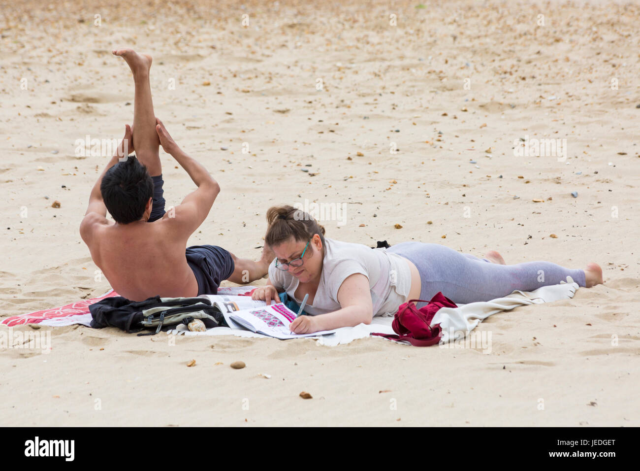 Bournemouth, Dorset, UK. 24th June, 2017. UK weather: overcast day with cooling breeze and sunny spells, as visitors head to the seaside. Couple on the beach, woman looking at magazine book, man doing exercises. Credit: Carolyn Jenkins/Alamy Live News Stock Photo