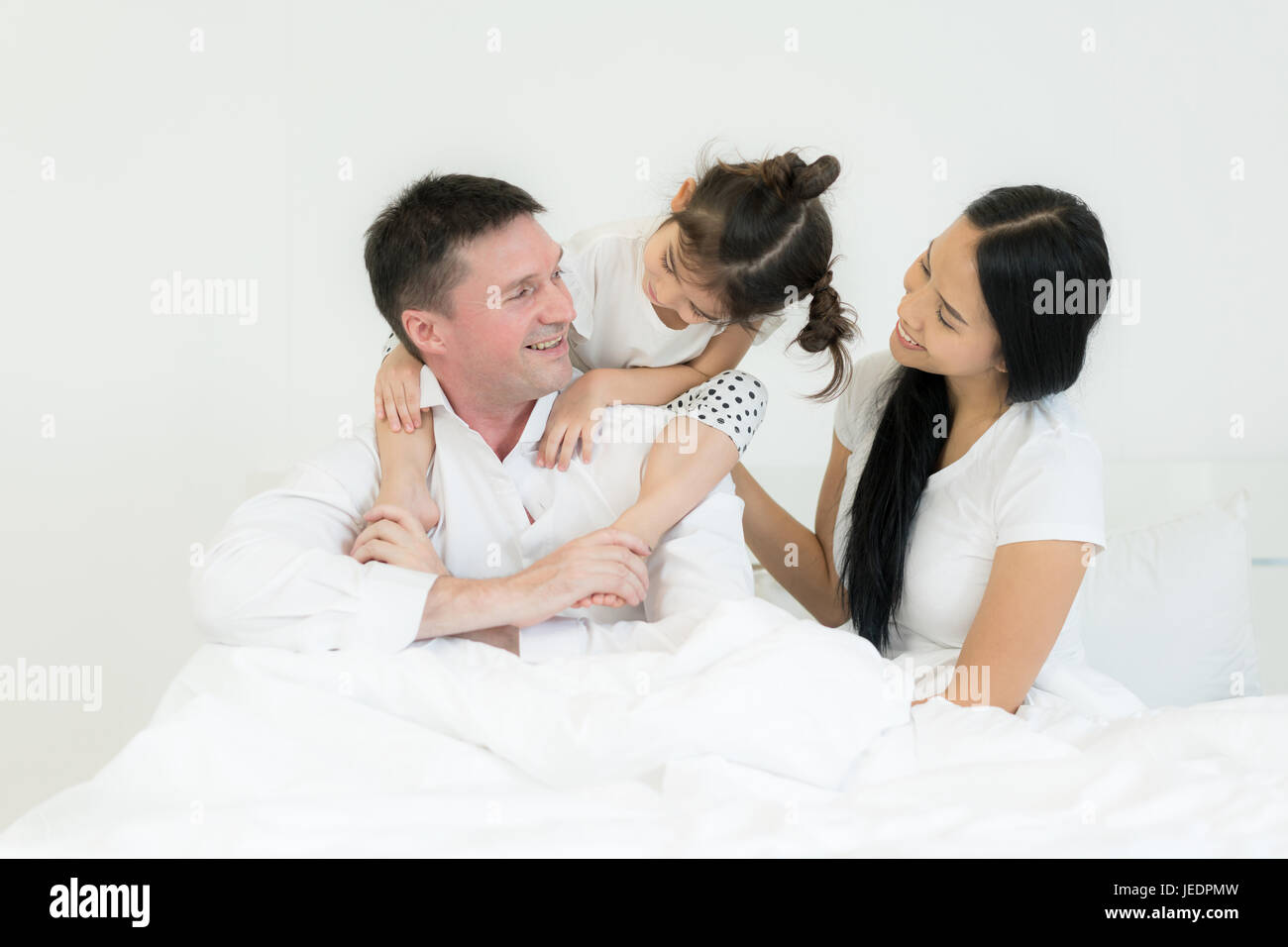Family with beautiful mother and handsome father with cute little daughter are talking and smiling while spending time together in bed. Happy family c Stock Photo