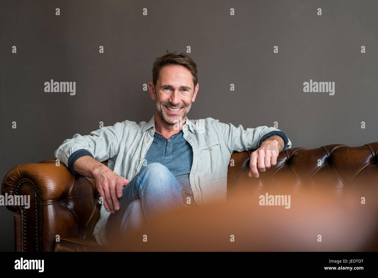 Portrait of smiling mature man sitting on leather couch Stock Photo - Alamy