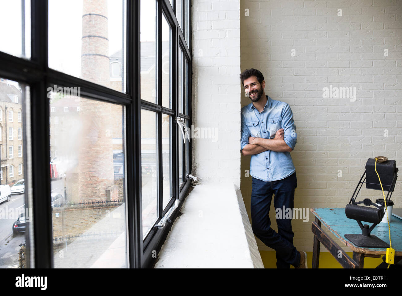 Smiling man leaning against a wall in his loft Stock Photo - Alamy