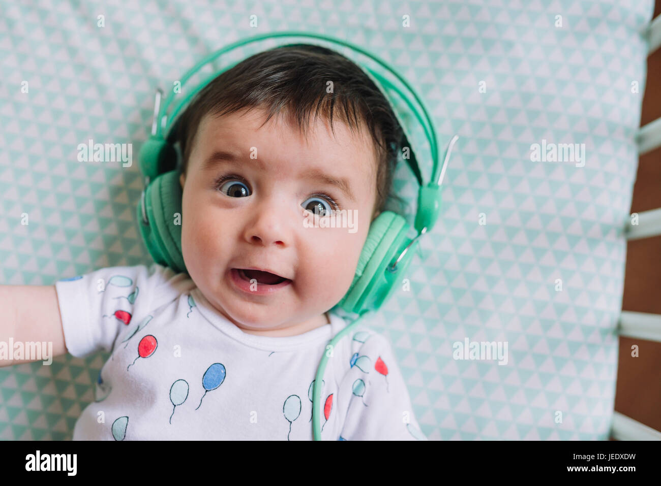 Portrait of baby girl with headphones lying in crib Stock Photo