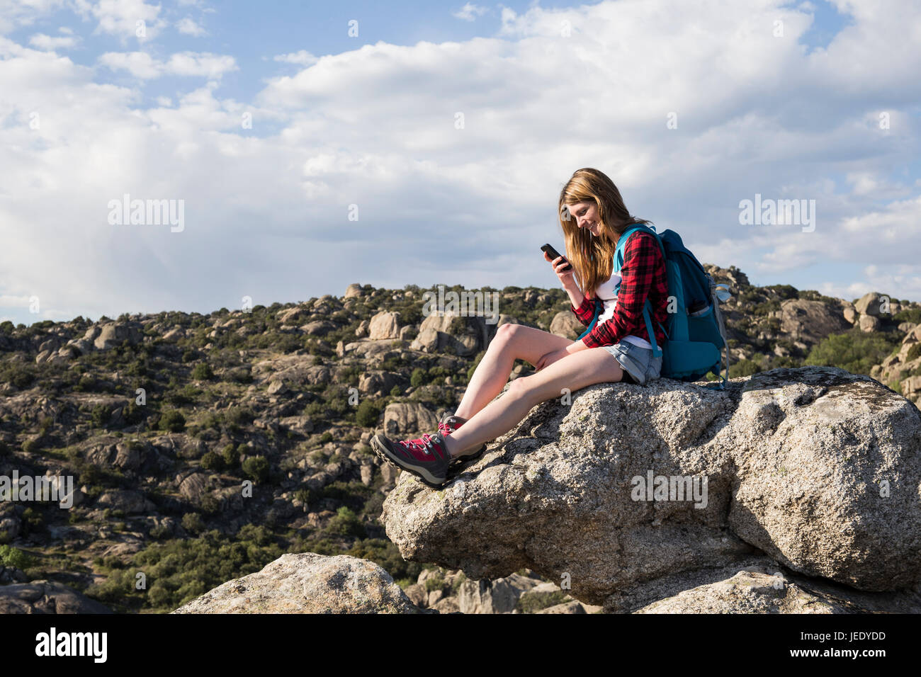 Spain, Madrid, young woman resting on a rock using her phone during a trekking day Stock Photo