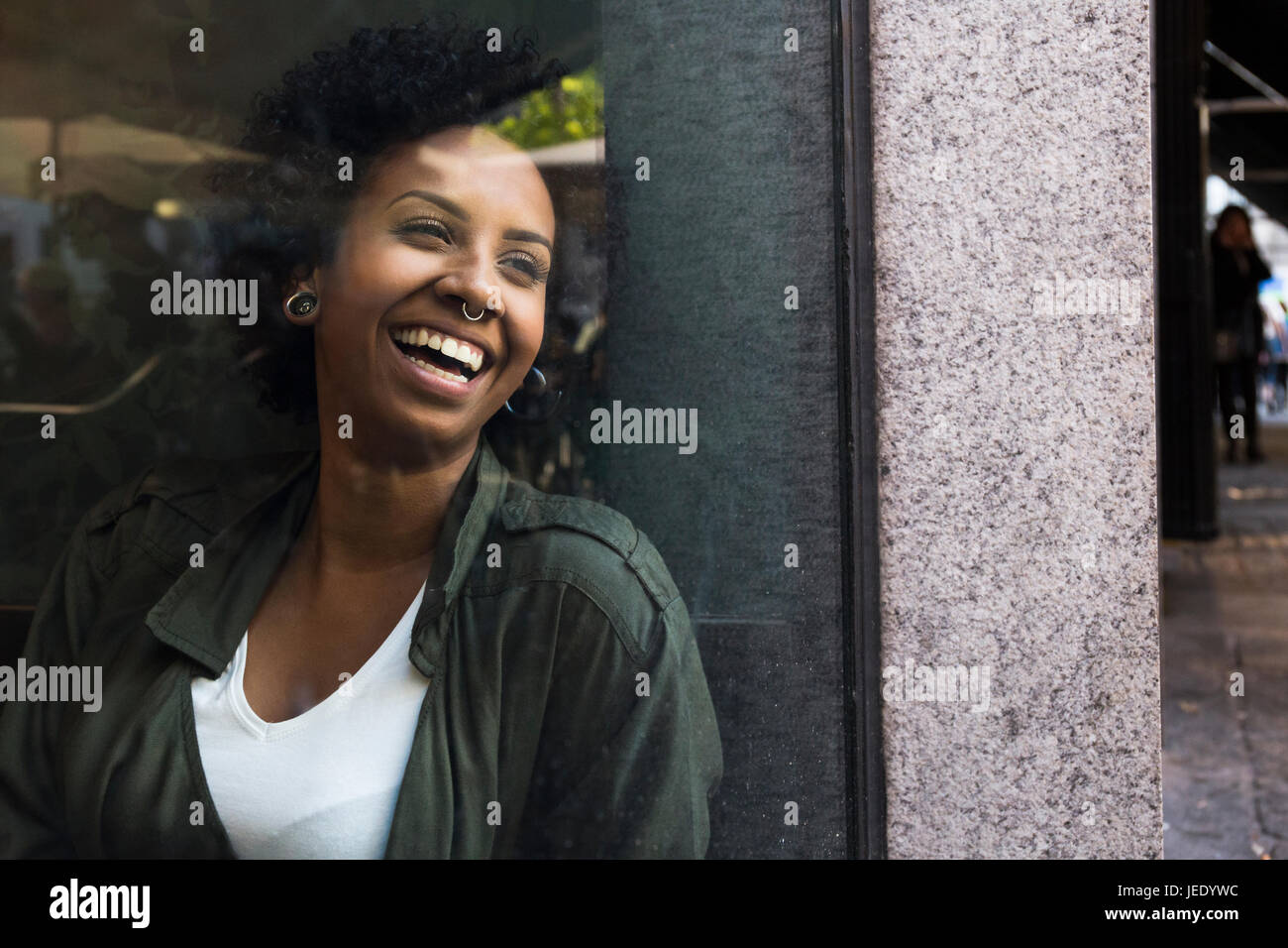 Portrait of laughing young woman looking through window of a cafe Stock Photo