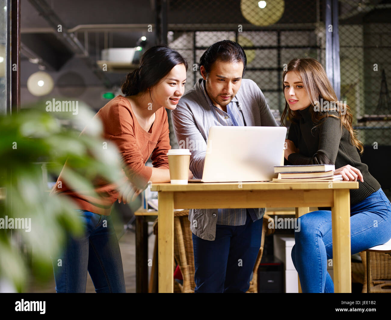 a team asian and caucasian entrepreneurs meeting in office discussing business using laptop computer. Stock Photo
