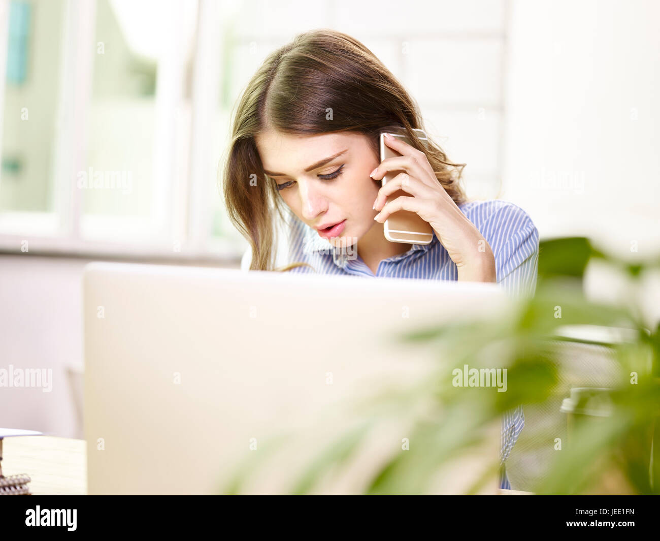 young caucasian female business executive working in office using mobile phone and laptop computer. Stock Photo