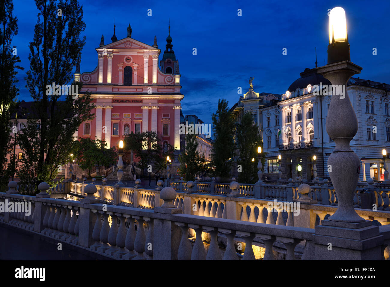 Lights on pink facade of Franciscan Church of the Annunciation and Central Pharmacy Preseren Square at dusk Triple Bridge Ljubljana Slovenia Stock Photo