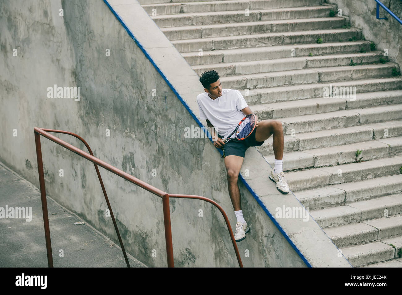 An athlete with a tennis racket sits on a concrete railing of steps ...