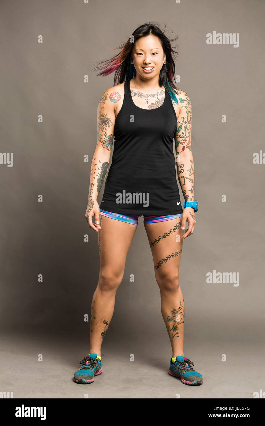 Athletic young asian woman with tattoos dressed in a black tank top and colored gym shorts smiles Stock Photo