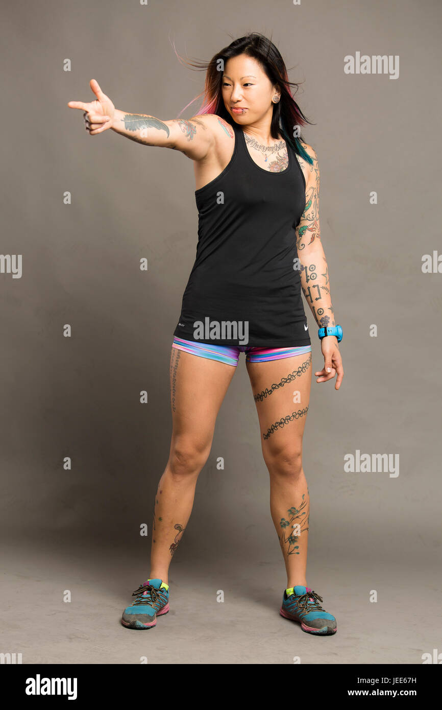 Athletic young asian woman with tattoos dressed in a black tank top and colored gym shorts smiles Stock Photo