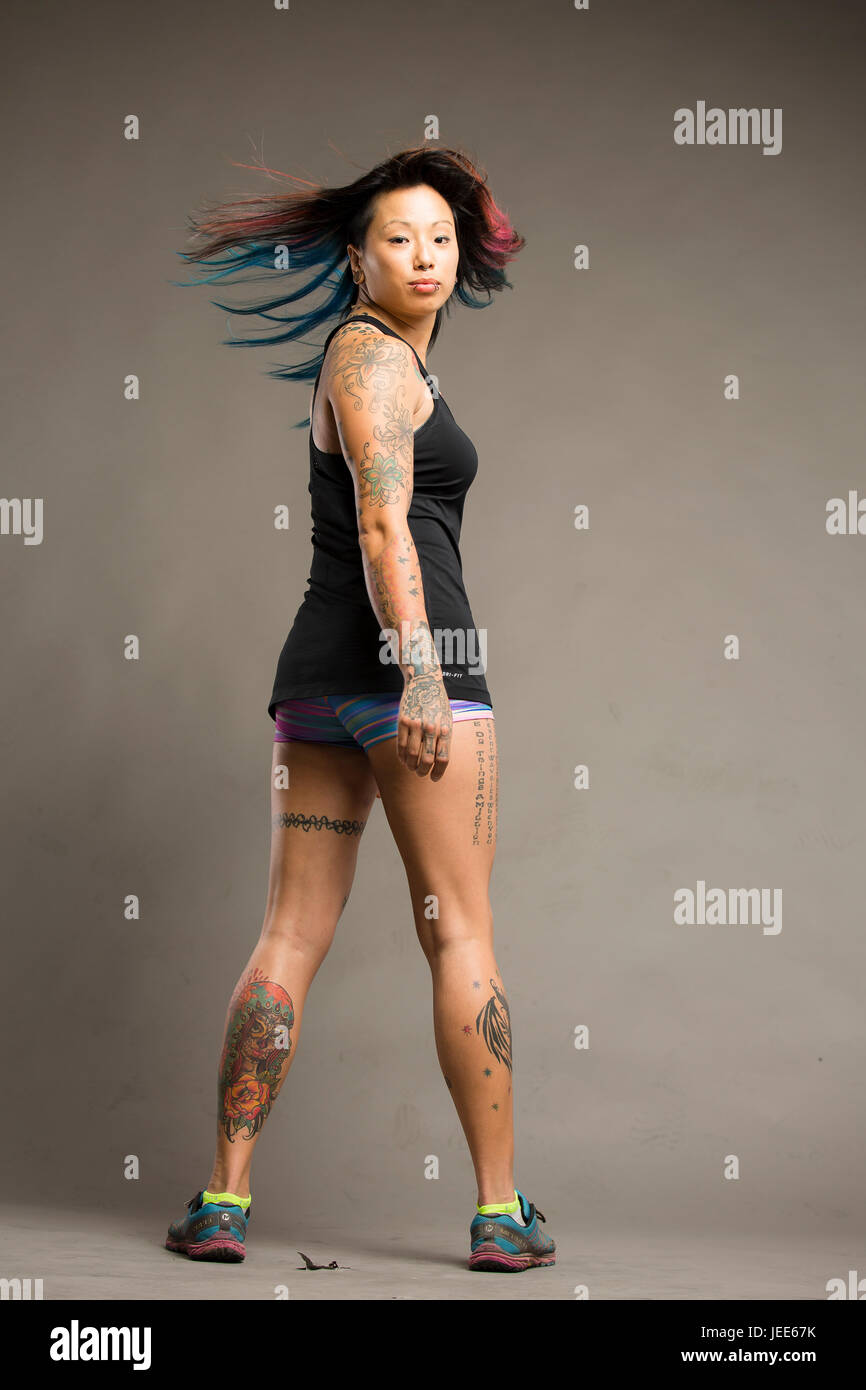 Athletic young asian woman with tattoos dressed in a black tank top and colored gym shorts smiles Stock Photo