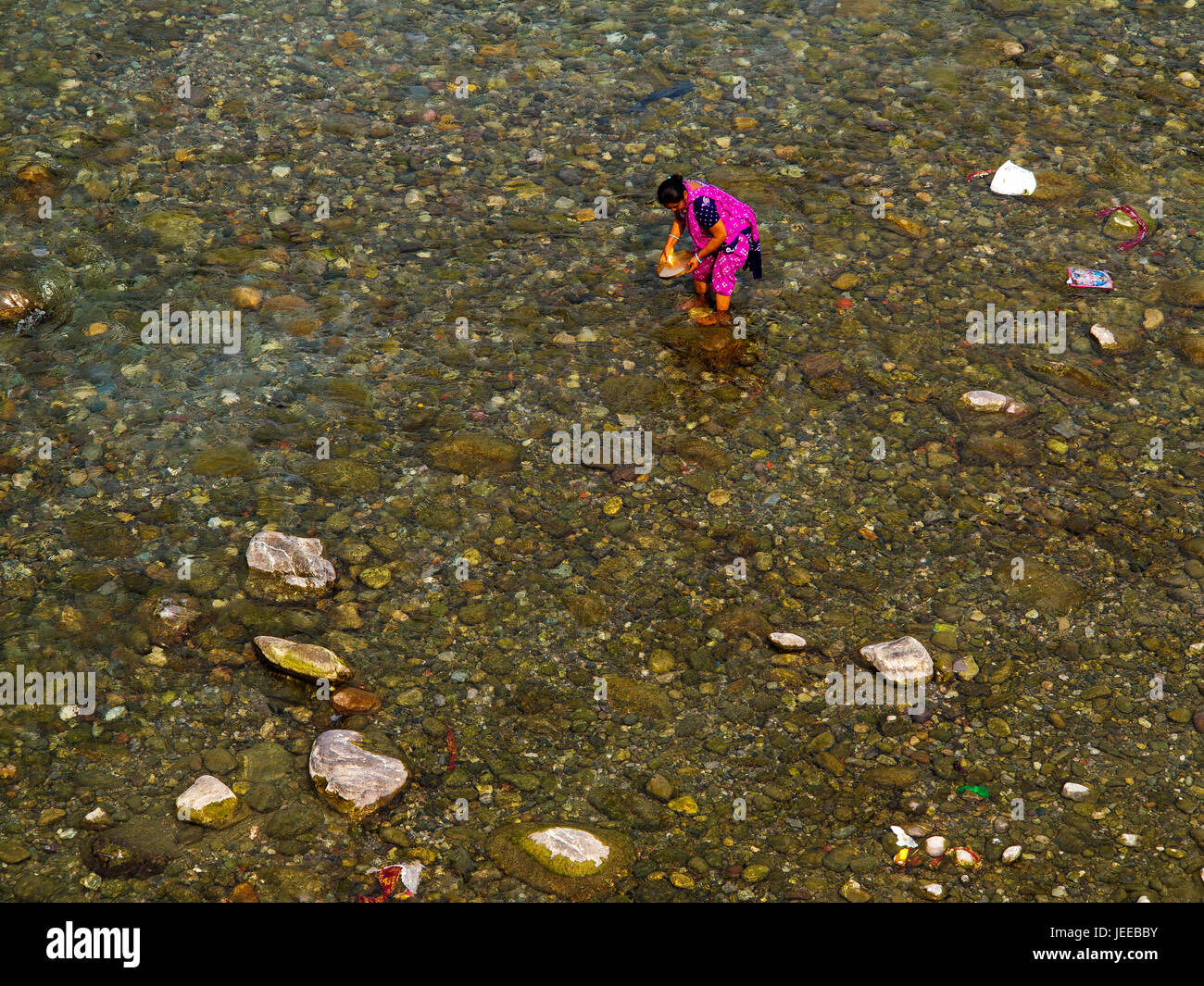 Indian woman in traditional colorfull clothes washing dishes in the Kosi River at Garjiya, Uttarakhand, India Stock Photo
